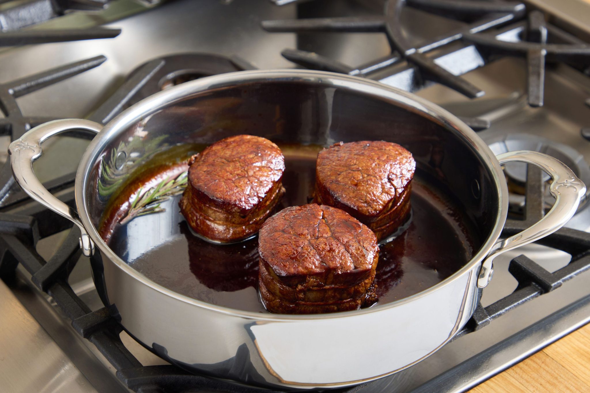 Filet mingon with demi-glace and sprig of rosemary in a Hestan pan on gas stove burner